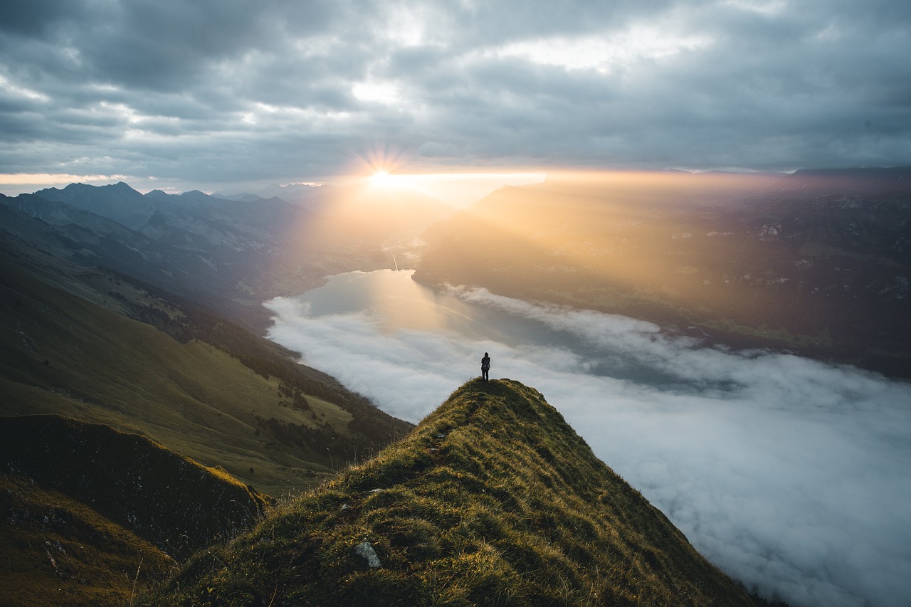 Person standing on top of a mountain looking over a cloud-filled valley